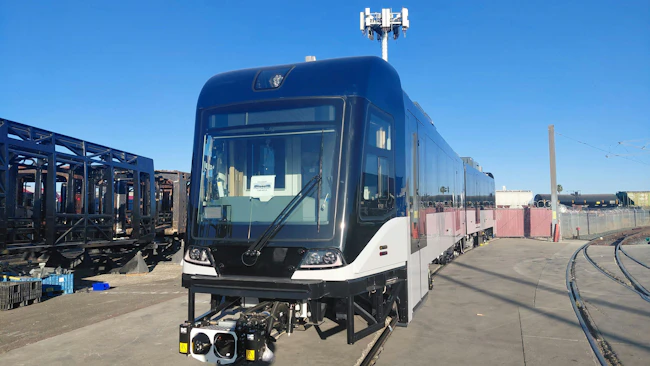 A new Siemens Mobility light-rail vehicle for the Greater Cleveland Regional Transit Authority (GCRTA) sits on a rail yard track under a clear blue sky, featuring a sleek black and white exterior with a modern cab design and roof-mounted equipment, surrounded by industrial yard infrastructure.