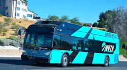 Victor Valley Transit Authority hydrogen fuel cell bus number 317 in a bold teal and black livery with 'Hydrogen Fuel Cell' lettering along the roofline navigates a desert community street in the Victor Valley area of Southern California under a clear blue sky.