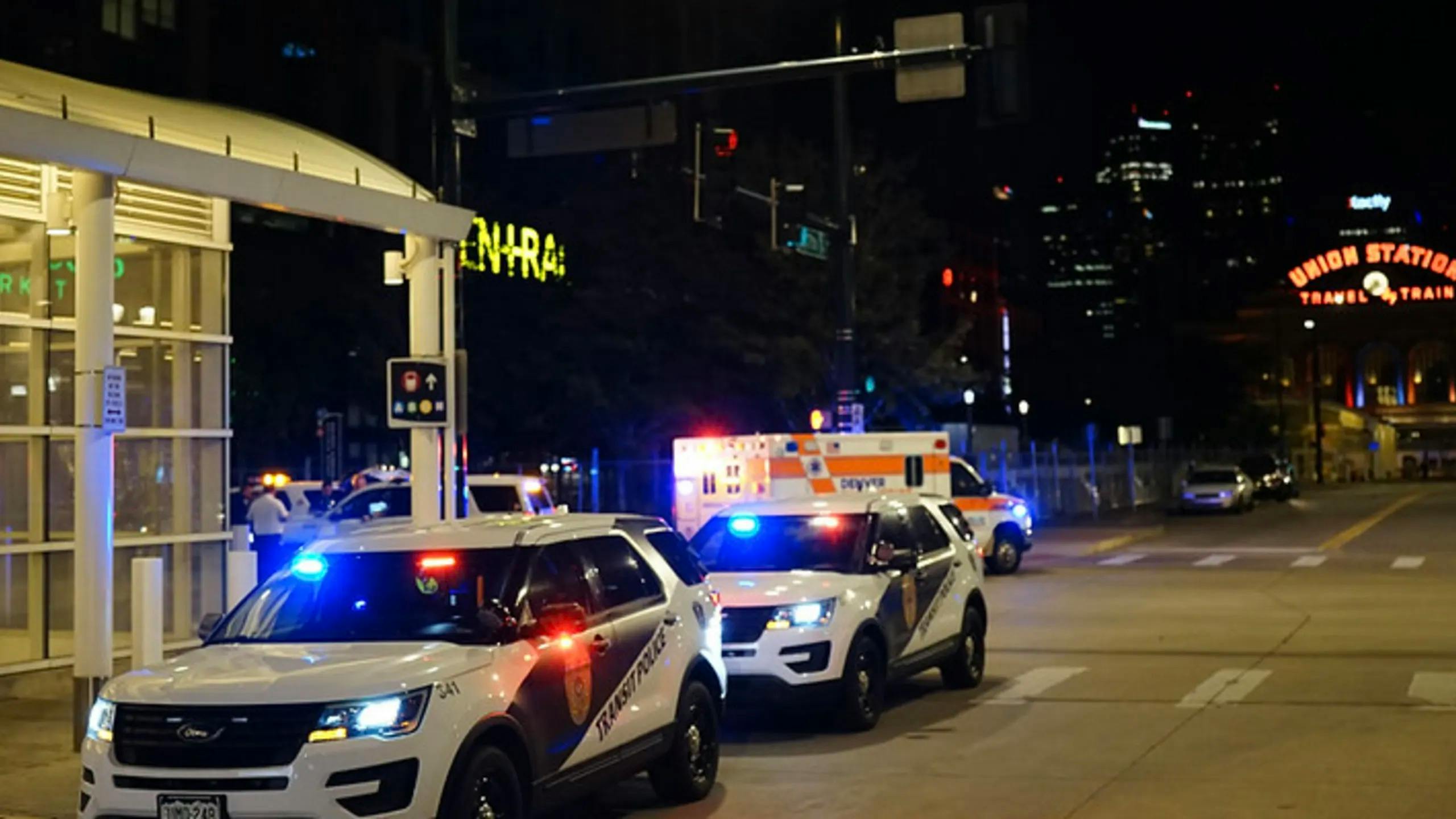 Multiple Transit Police vehicles and an ambulance with emergency lights activated respond to an incident near a station at night, with the illuminated Union Station sign visible in the background.