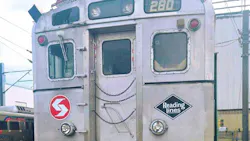 A close-up of the rear end of a retired SEPTA Silverliner commuter rail car number 280, showing the original SEPTA logo and a Reading Lines diamond emblem on its stainless steel exterior, with chain-secured doors and a newer SEPTA train visible in the background at a rail yard.