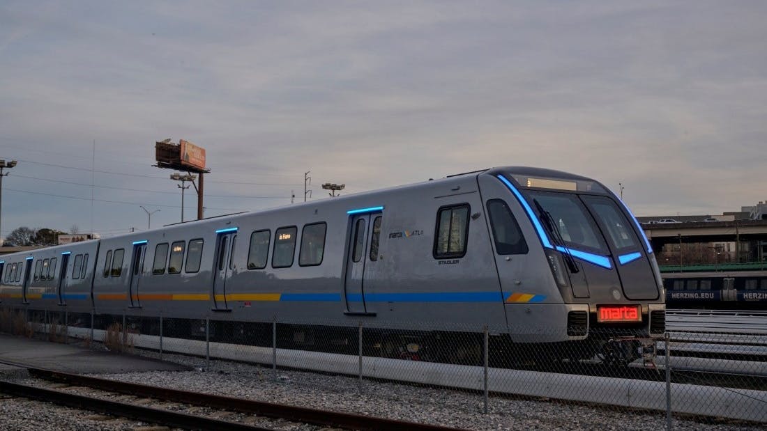 A MARTA Stadler-built railcar in a sleek gray livery with blue LED accent lighting and a blue and gold horizontal stripe sits in a rail yard in Atlanta, displaying the MARTA name on its red LED destination board under an overcast sky.