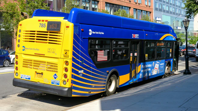 Rear-angled view of an MTA New York City Bus, numbered 785 running route B63, showing its blue and yellow livery, CNG clean-air technology signage, and a lottery ad wrap, parked along a city street.