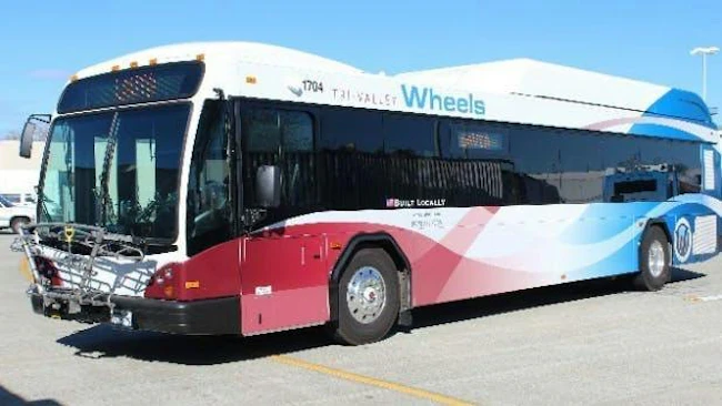 Tri-Valley Wheels bus number 1704 in a white, red and blue wave livery with 'Built Locally' branding and a front-mounted bicycle rack, parked in a transit lot in the Tri-Valley area of California's Alameda County.