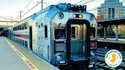 An NJ Transit bi-level rail car, numbered 7011, sits at a platform beside a 'Mind the Gap' warning strip, with the Garden State Initiative logo overlaid in the corner.
