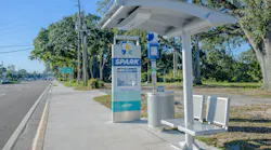 A PSTA SPARK bus rapid transit stop on 18th Avenue South, featuring Tolar's branded totem sign with route map and a real-time e-paper passenger information display, alongside a shaded shelter with metal benches along the roadside.