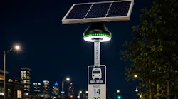 Connectpoint's HALO solar-powered lighting system illuminates a bus stop sign for routes 14 and 29 at night, with a city skyline and empty street visible in the background.