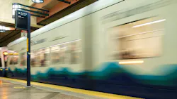 Long-exposure photo of a Sound Transit Link light rail train, in blue and white livery with a wave graphic, pulling out of a station past a 'Bus Bay D' wayfinding sign for Route 550 to Bellevue.