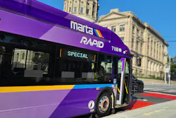 MARTA Rapid bus number 7108, a New Flyer Xcelsior in a bold purple, gold, and blue livery displaying 'Special' on its destination board, stops at a red-painted bus rapid transit lane in front of the Georgia State Capitol building in downtown Atlanta under a clear blue sky