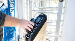 A rider taps a smartphone against a Justride fare validator at a turnstile gate, displaying a QR configuration screen, with an accessible-entrance sign visible in the background.