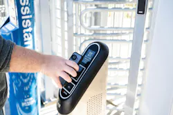 A rider taps a smartphone against a Justride fare validator at a turnstile gate, displaying a QR configuration screen, with an accessible-entrance sign visible in the background.