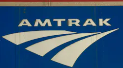 Close-up of the Amtrak logo, showing the wordmark and arrow-shaped graphic in white against a blue background on the side of a rail car.