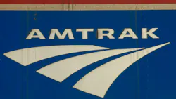 Close-up of the Amtrak logo, showing the wordmark and arrow-shaped graphic in white against a blue background on the side of a rail car.
