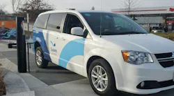 A white Dodge Grand Caravan branded as 'Salem Skipper' with blue wave graphics is parked at a curb near a charging station and gas station in the background.