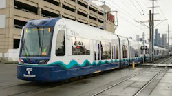 A Sound Transit Link light-rail vehicle, car 282B, travels on tracks past the SODO neighborhood in Seattle, with the city skyline visible in the background.