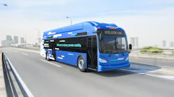 Rendering of a New Flyer Xcelsior CNG bus in blue and white livery, displaying 'Welcome to cleaner, smarter mobility' along its side, traveling on an elevated highway with a city skyline in the background.