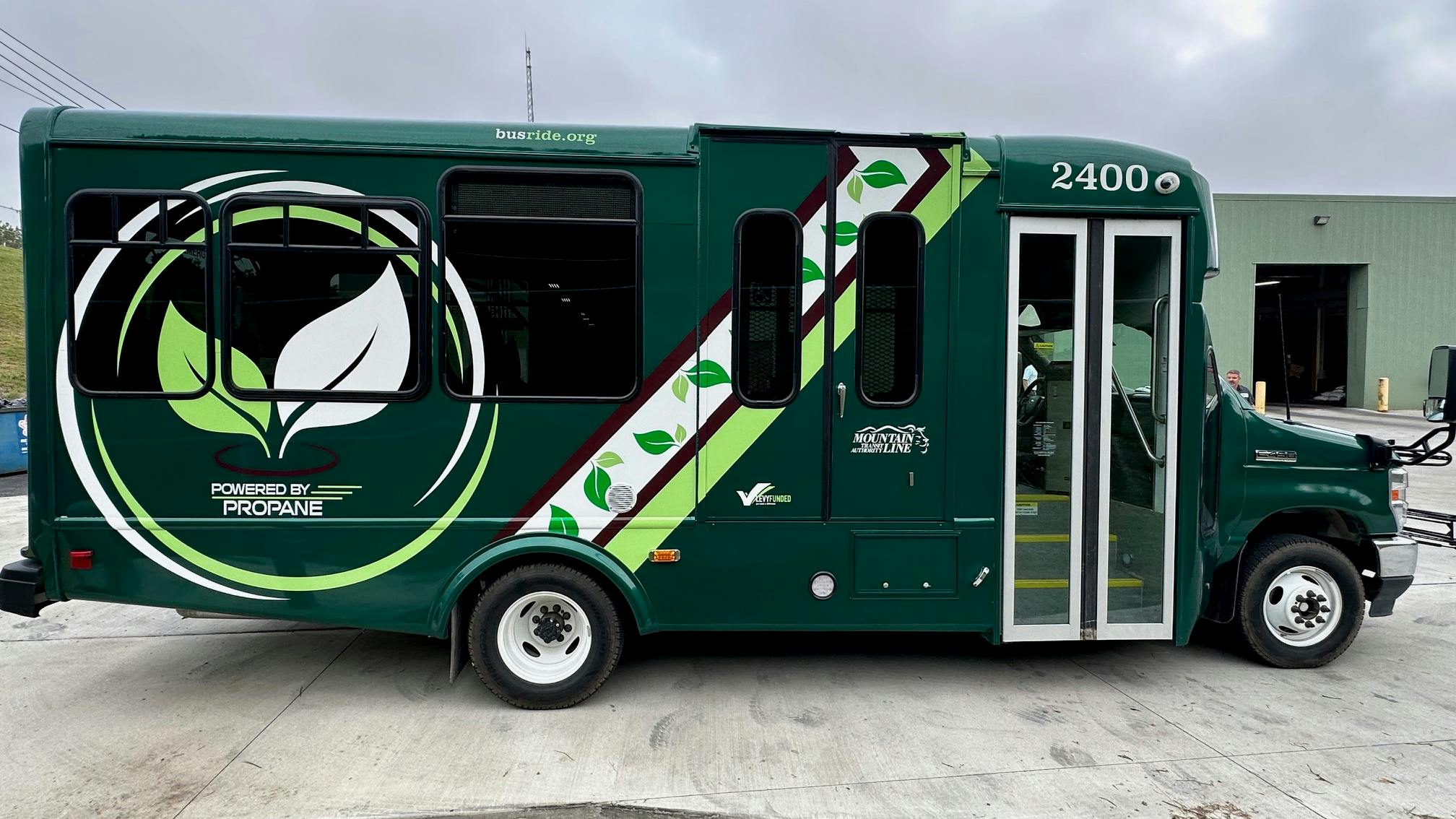 A green Mountain Line Transit Authority bus, unit 2400, featuring 'Powered by Propane' branding, is parked outside a maintenance facility in West Virginia.