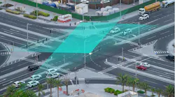 An aerial view of a busy intersection shows a teal-colored graphic overlay illustrating vehicle detection and signal timing technology used to coordinate traffic flow.