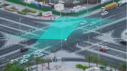 An aerial view of a busy intersection shows a teal-colored graphic overlay illustrating vehicle detection and signal timing technology used to coordinate traffic flow.