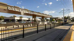 The newly opened Dos Rios light-rail station, with an overhead canopy displaying the station name, a light-rail train approaching on the tracks, and a black metal fence lining the platform.