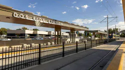 The newly opened Dos Rios light-rail station, with an overhead canopy displaying the station name, a light-rail train approaching on the tracks, and a black metal fence lining the platform.