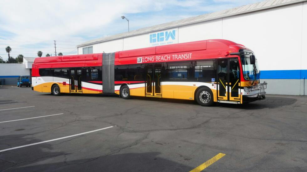 A red, white and yellow Long Beach Transit articulated bus, built by Complete Coach Works, parked outside the manufacturer's facility.