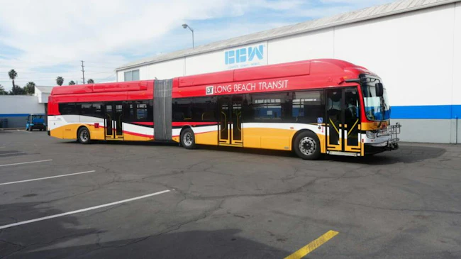 A red, white and yellow Long Beach Transit articulated bus, built by Complete Coach Works, parked outside the manufacturer's facility.