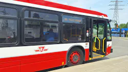 A TTC bus, numbered 3365 and signed '66 Prince Edward,' stands with its doors open at a curb, showing the agency's logo and priority seating signage, with a streetcar and power transmission towers visible in the background.
