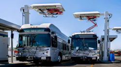 Two L.A. Metro electric buses are parked beneath overhead pantograph charging stations at El Monte Station in California.