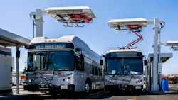 Two L.A. Metro electric buses are parked beneath overhead pantograph charging stations at El Monte Station in California.