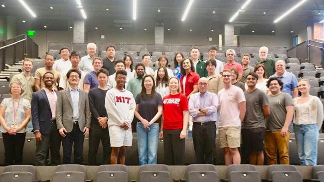 A large group of faculty, researchers and students from the MIT Transit Lab pose together in a lecture hall, with several wearing MIT-branded clothing.