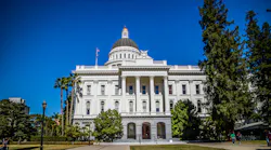 The California State Capitol building in Sacramento, showing its white Corinthian columns, domed rotunda topped with a gold finial, and surrounding palm trees and lawn.