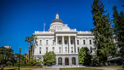 The California State Capitol building in Sacramento, showing its white Corinthian columns, domed rotunda topped with a gold finial, and surrounding palm trees and lawn.