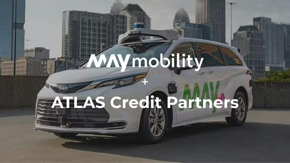 A May Mobility autonomous vehicle is shown with a city skyline in the background, overlaid with text announcing a partnership between May Mobility and ATLAS Credit Partners.