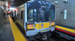 An MTA Long Island Rail Road train, car 7174, stops at Jamaica station with a conductor standing on the platform near the open doors.