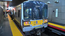 An MTA Long Island Rail Road train, car 7174, stops at Jamaica station with a conductor standing on the platform near the open doors.