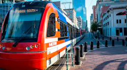 A Houston Metro Rail light rail train, numbered 209 and signed 'Fannin South,' travels down a brick-paved downtown street lined with historic and modern buildings.