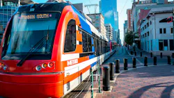 A Houston Metro Rail light rail train, numbered 209 and signed 'Fannin South,' travels down a brick-paved downtown street lined with historic and modern buildings.