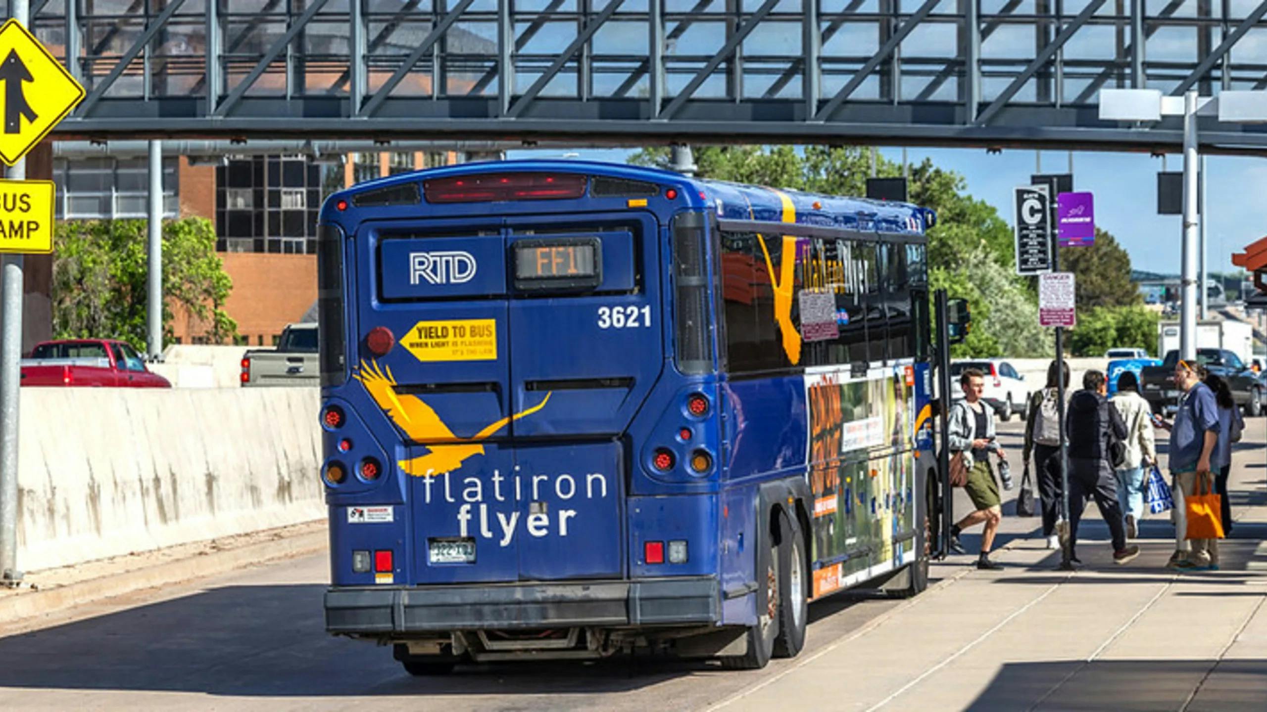 A Denver RTD Flatiron Flyer bus, unit 3621, on route FF1, loads passengers at a bus ramp station beneath a pedestrian overpass.