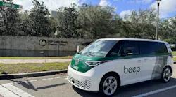 A white and green Beep-branded Volkswagen ID. Buzz van is parked on a street in front of the UCF Lake Nona Cancer Center sign, with a Sanger Road street sign visible above.