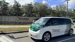 A white and green Beep-branded Volkswagen ID. Buzz van is parked on a street in front of the UCF Lake Nona Cancer Center sign, with a Sanger Road street sign visible above.