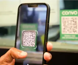 A hand holds a smartphone up to scan a green Convo-branded QR code sign, with the code framed on the phone's screen.
