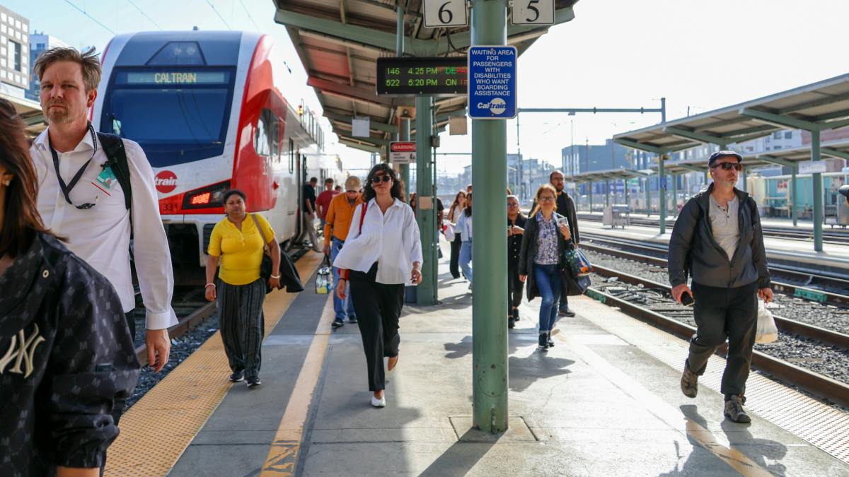 Caltrain passengers walk among the platform near a waiting train.
