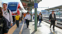 Caltrain passengers walk among the platform near a waiting train.