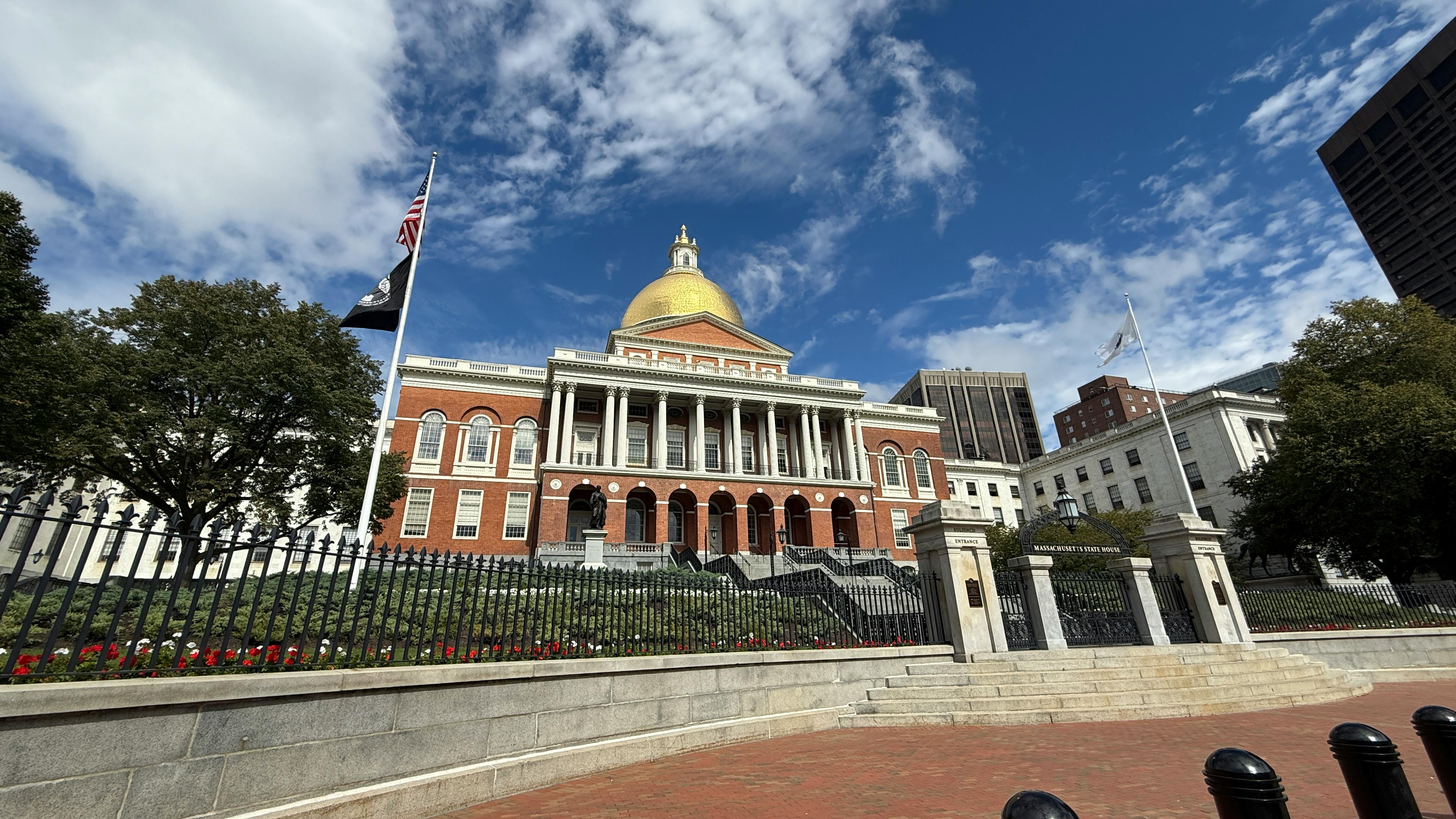 Exterior view of the Massachusetts State House, with its gold dome, under a partly cloudy blue sky.