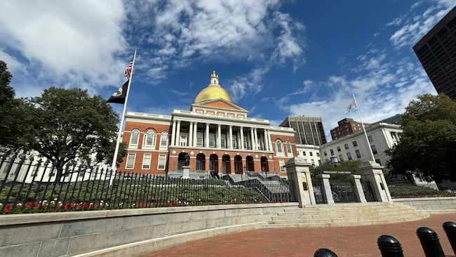 Exterior view of the Massachusetts State House, with its gold dome, under a partly cloudy blue sky.