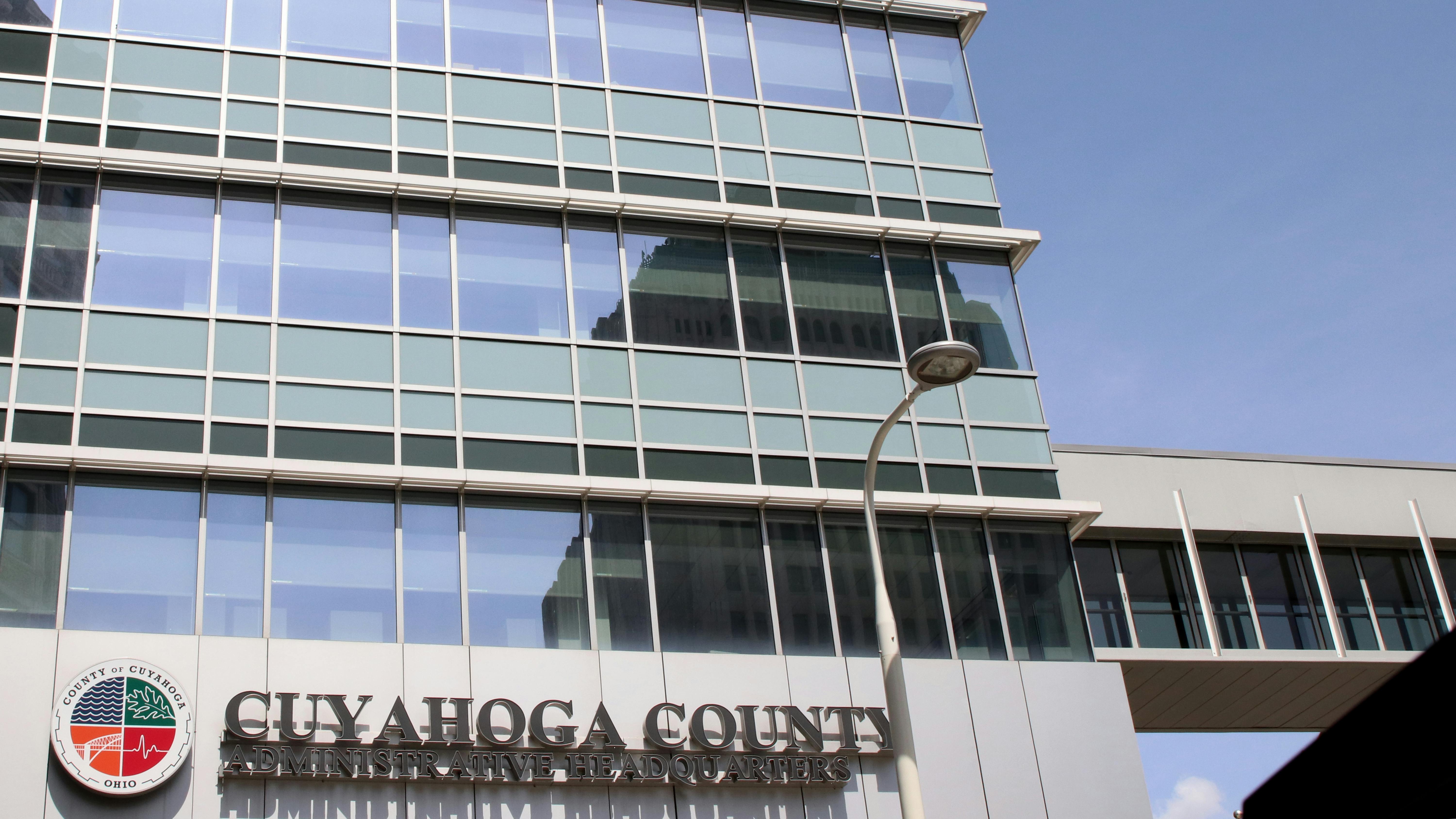 Upward view of the Cuyahoga County Administrative Headquarters building, a glass office tower, with its name on a sign near the entrance.