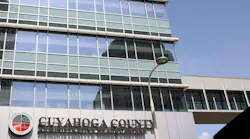 Upward view of the Cuyahoga County Administrative Headquarters building, a glass office tower, with its name on a sign near the entrance.