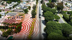 An aerial view of a passenger train traveling down a straight track beside a residential neighborhood, with a red concentric-ring graphic radiating across the nearby homes to suggest noise or vibration.