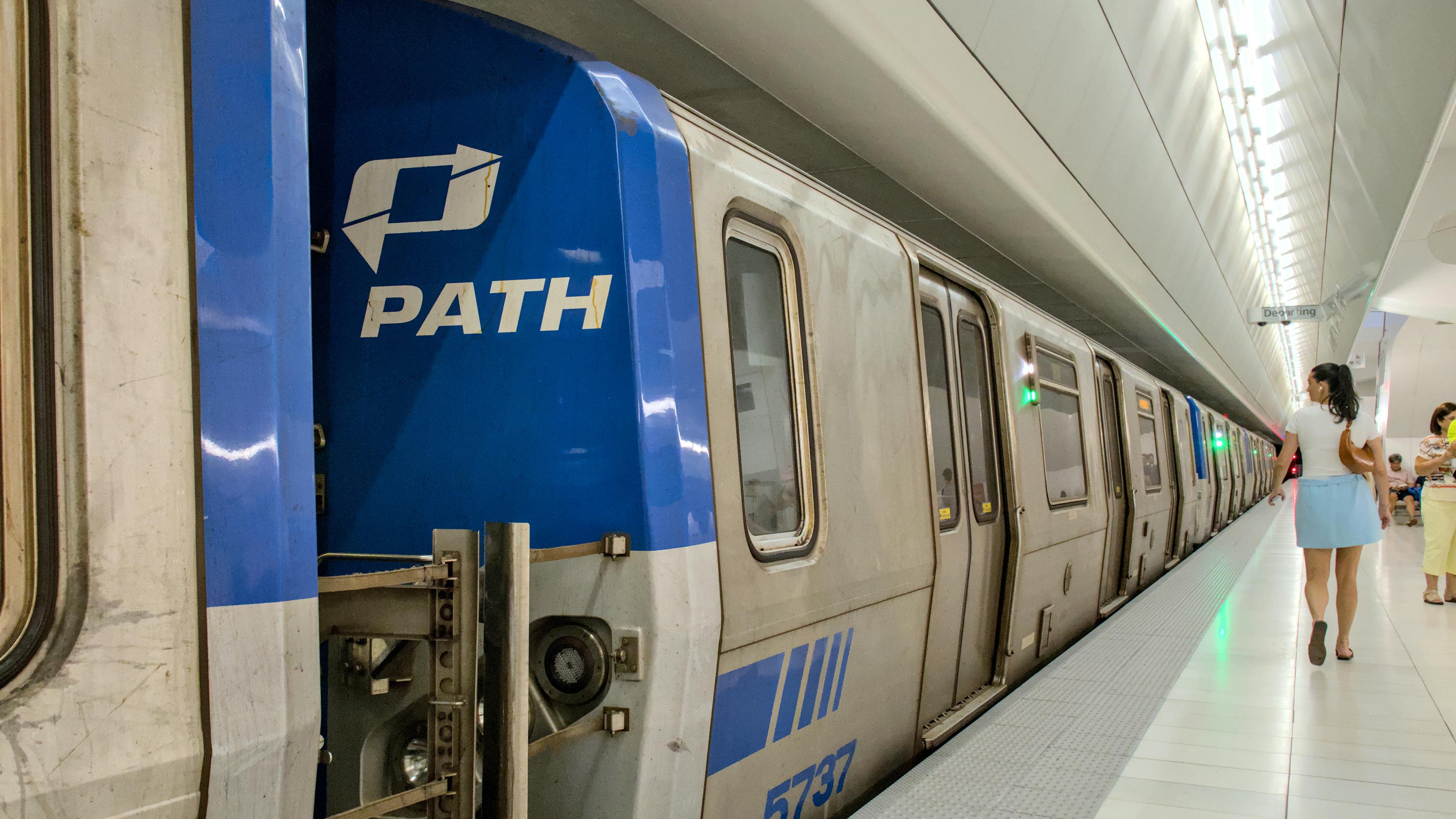 A PATH train is photographed in a station with a logo showing on the front of the train car as someone walks by.