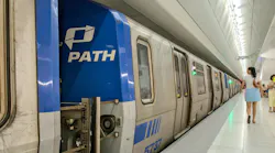 A PATH train is photographed in a station with a logo showing on the front of the train car as someone walks by.